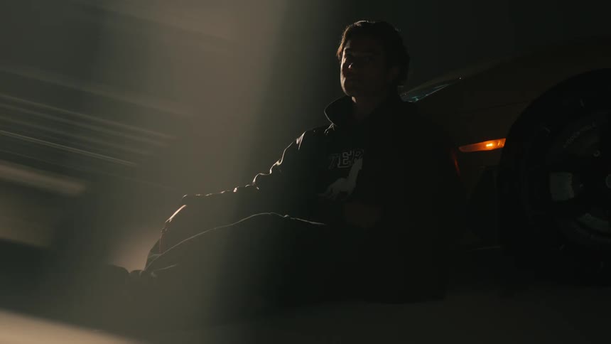 A man is sitting by a sport car in a garage