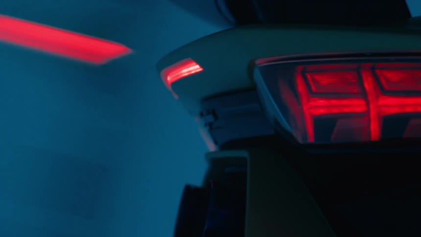 Closeup of a sports car rear spoiler and tail lights in a blue lit garage