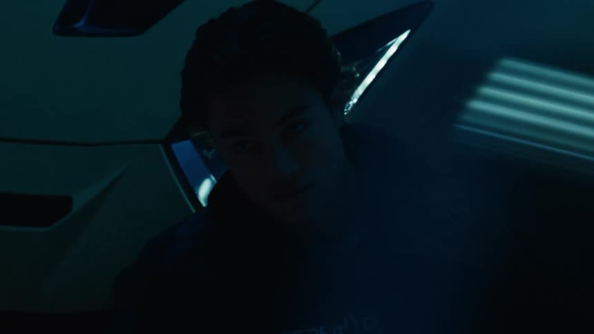 Red and blue lighting shines onto a man leaning against a car