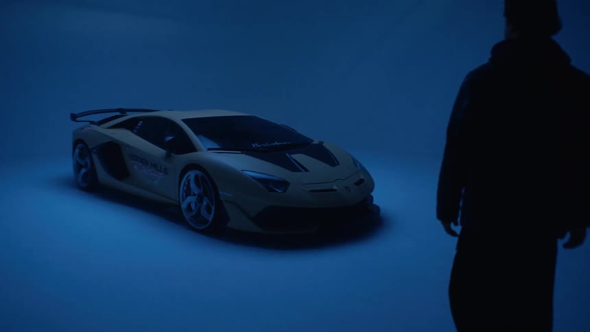 Man approaches a sports car parked indoors and lit by blue lighting