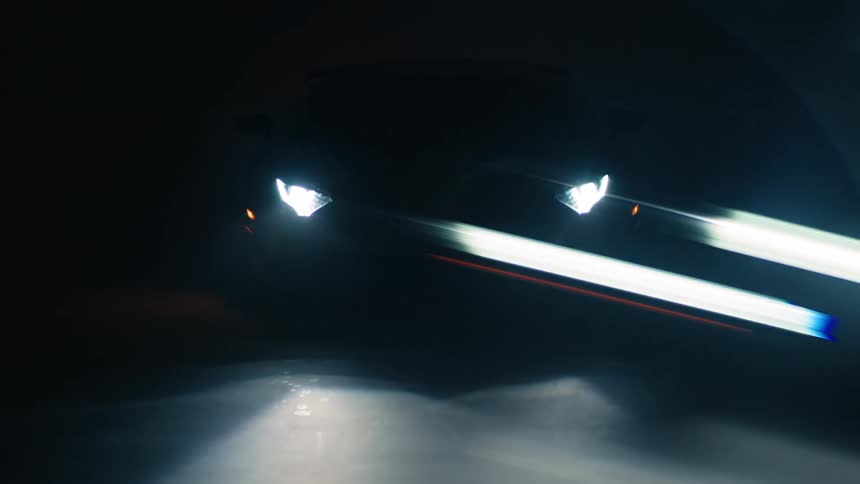 A sleek sports car with glowing headlights appears in a dark bluelit setting