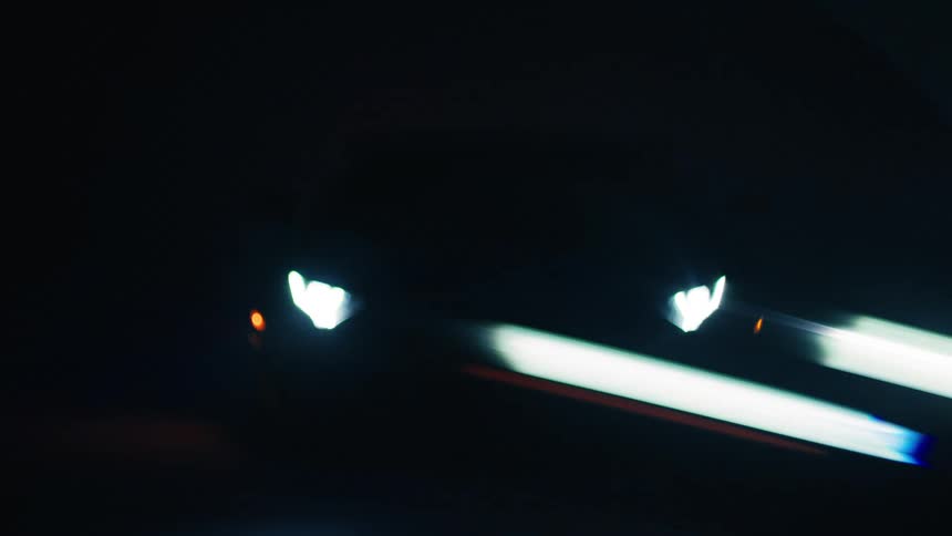 A sleek sports car emerges from shadows headlights piercing the dark