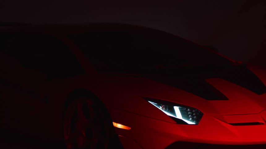 A modern sports car glows with red illumination in a dimly lit room