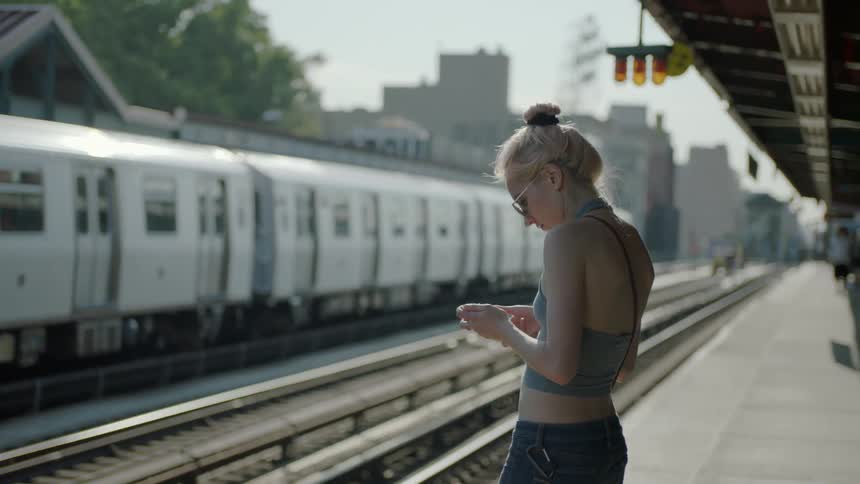 A woman uses her phone while waiting at a train station