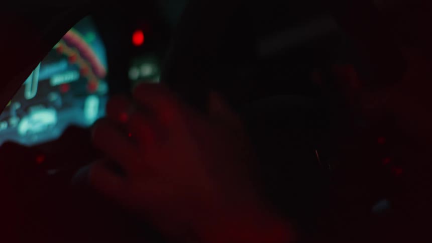 A persons hands holding a steering wheel and turning it sideways in a car that has a dark interior