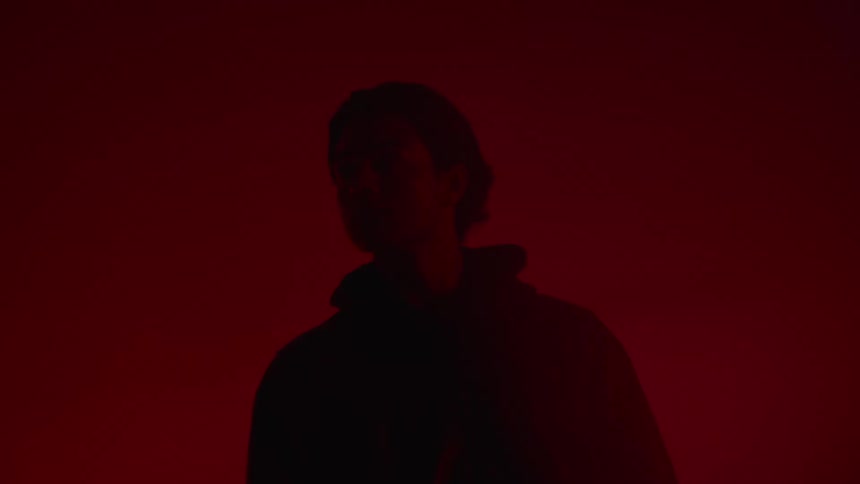 A man in a leather jacket is walking towards a sports car while in a garage