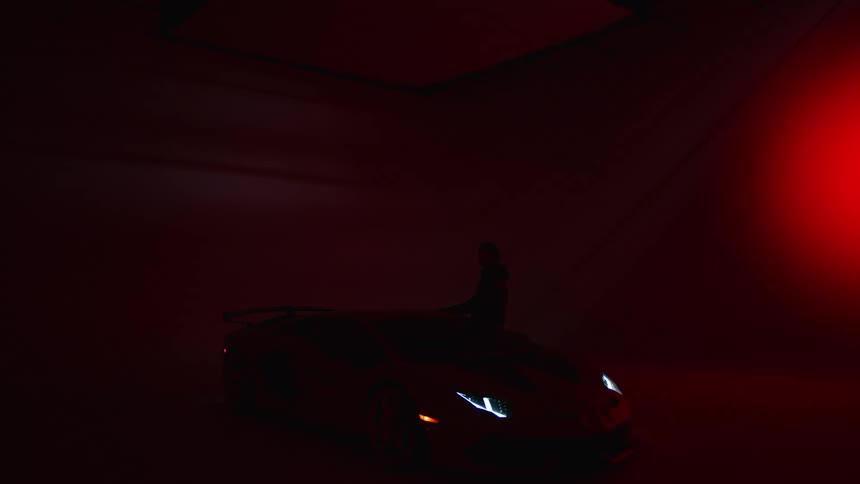 A man is standing near a sports car while a red spots light is moving on the nearby wall