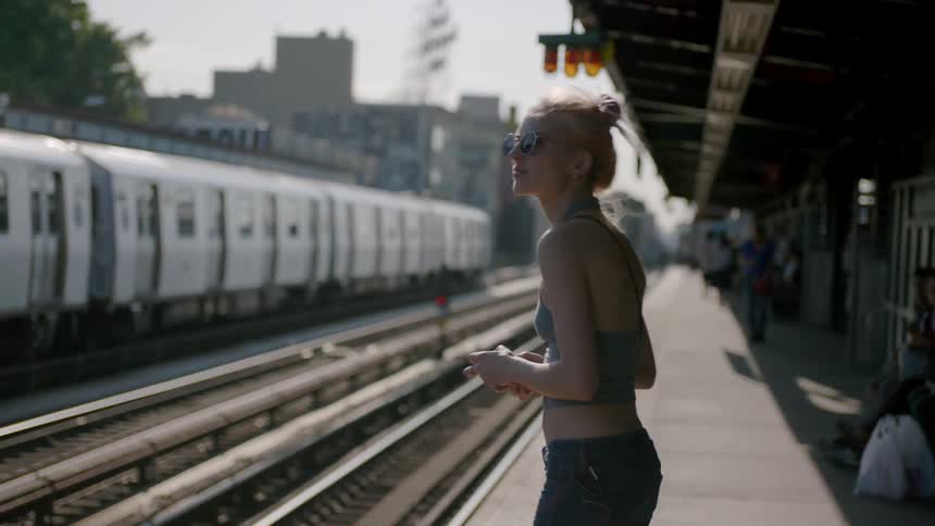 Woman in a grey tube top checks phone while waiting at train station