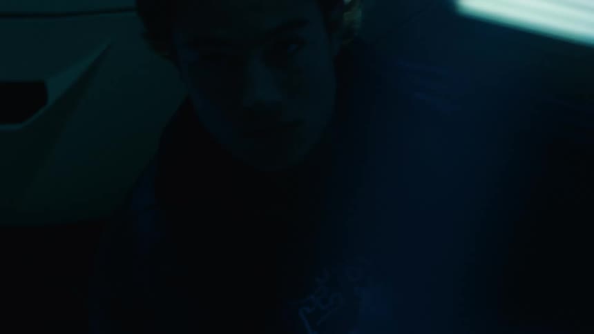Man partially illuminated by red and blue light adjusts his jacket next to a sports car