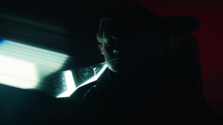 Young person leans against a car parked with its headlights on