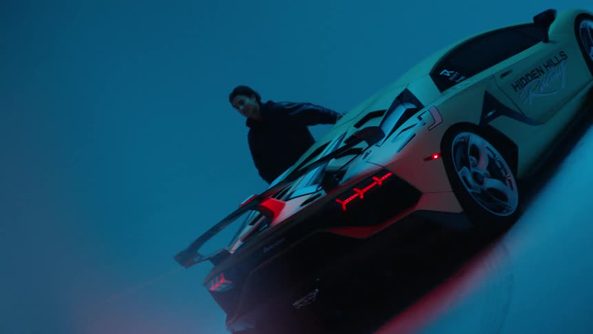 A man is standing next to a white sports car while red and blue lights flash chaotically