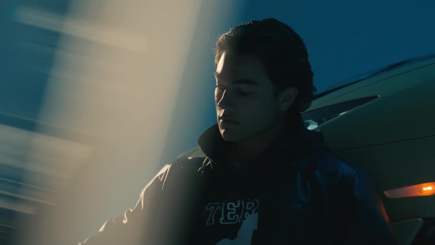 Man sitting on the floor leans against a parked car