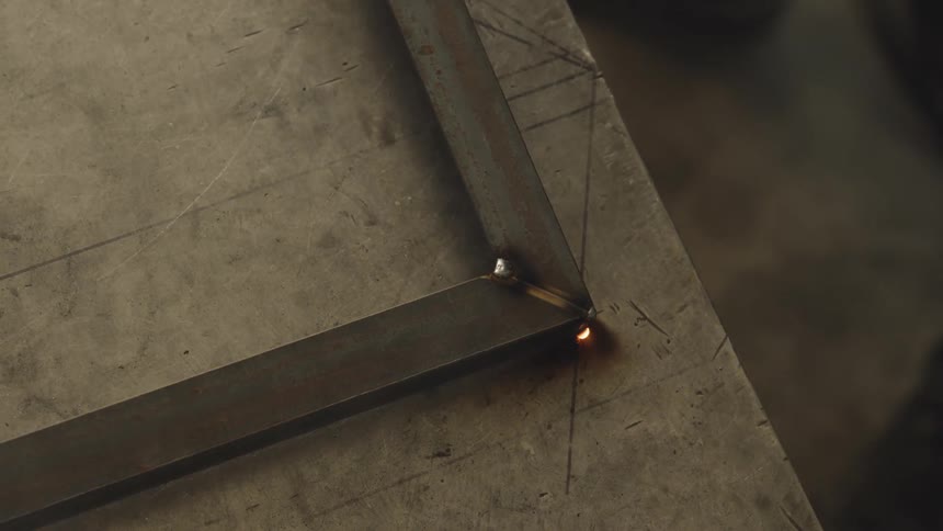 An arc welder joins two pieces of metal with a bright blue light