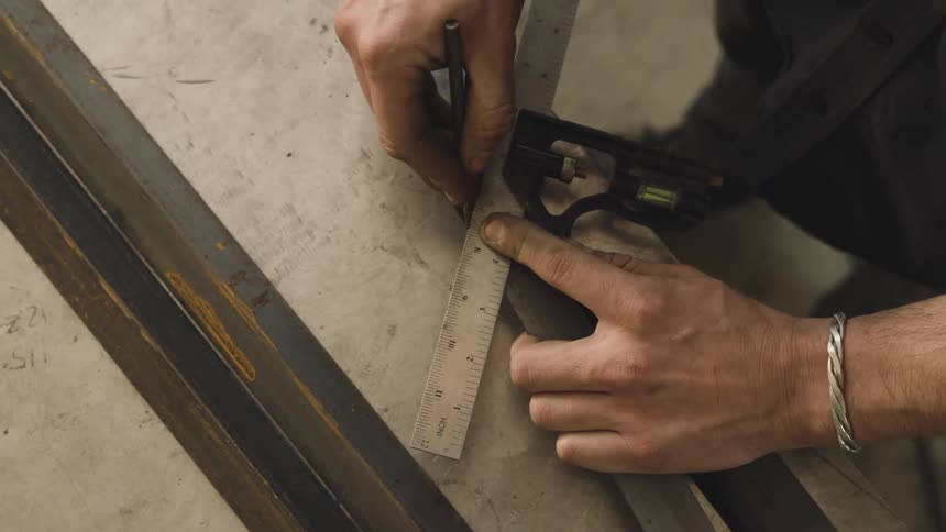 A man measuring and marking a metal bar with a ruler and a metal pencil