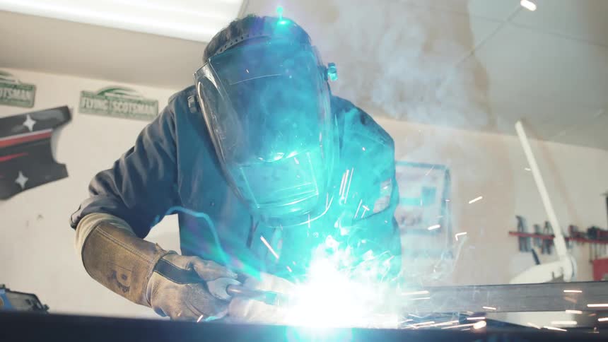 Welder wearing a protective mask works with sparks and intense light in a brightly lit workshop
