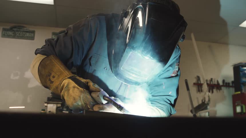 A person wearing a protective helmet is welding and releasing several sparks that are reflecting on his helmet