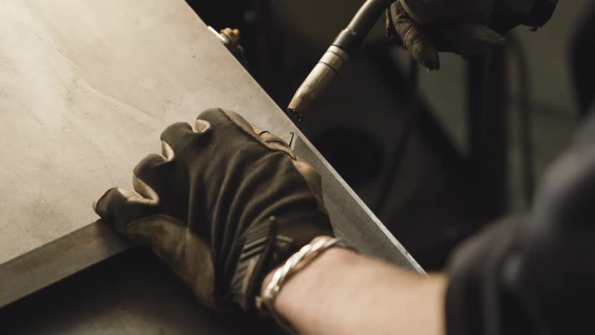 A human hand wearing black gloves using a soldering iron to solder a metal object and releasing several blue sparks