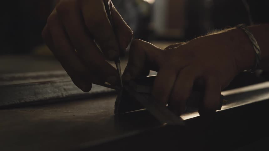 A man making markings on an iron bar using a metal ruler and a metal scribe pencil