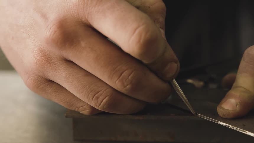 A man using a metal ruler and a metal pencil to make markings on an iron bar