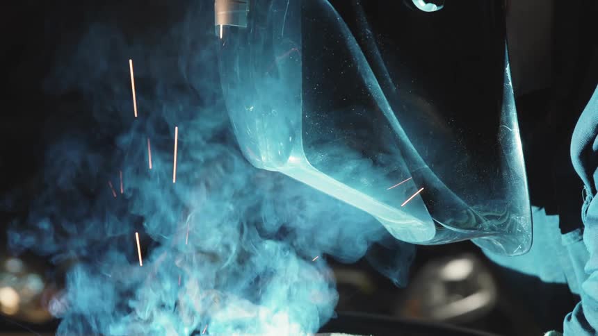 Metalworker with protective mask in front of a light with sparks and smoke