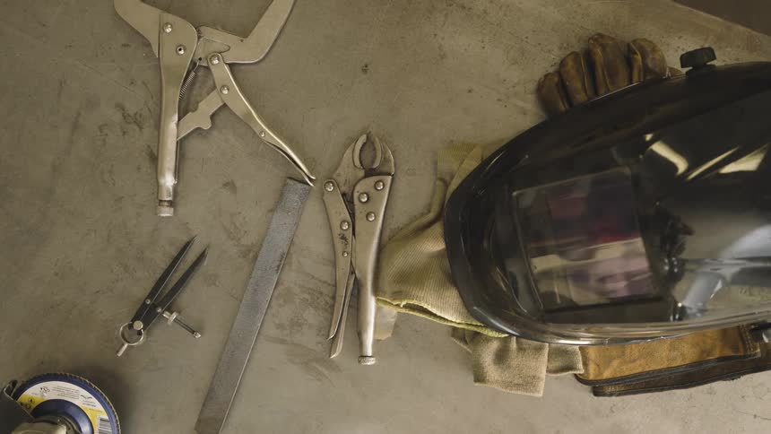 A welding helmet rests on work gloves amidst various metalworking tools on a workbench
