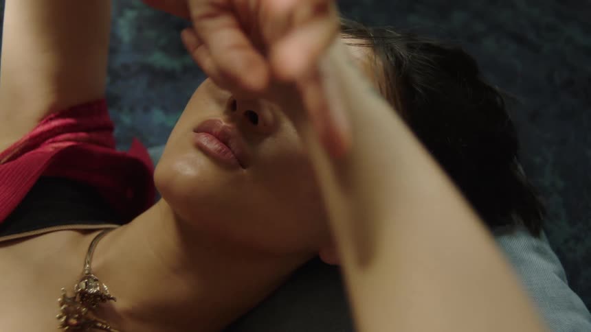 A woman lies on her back thoughtfully gazing upward while twisting her hands