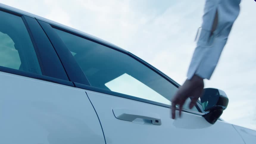 A man in a white shirt opens a white car door under a bright sky