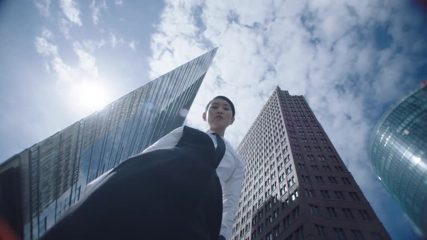 Confident businesswoman shot from low angle with skyscrapers and cloudy sky