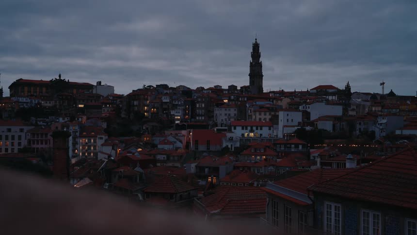 Moody dusk cityscape with dense rooftops and a tall clock tower in the background