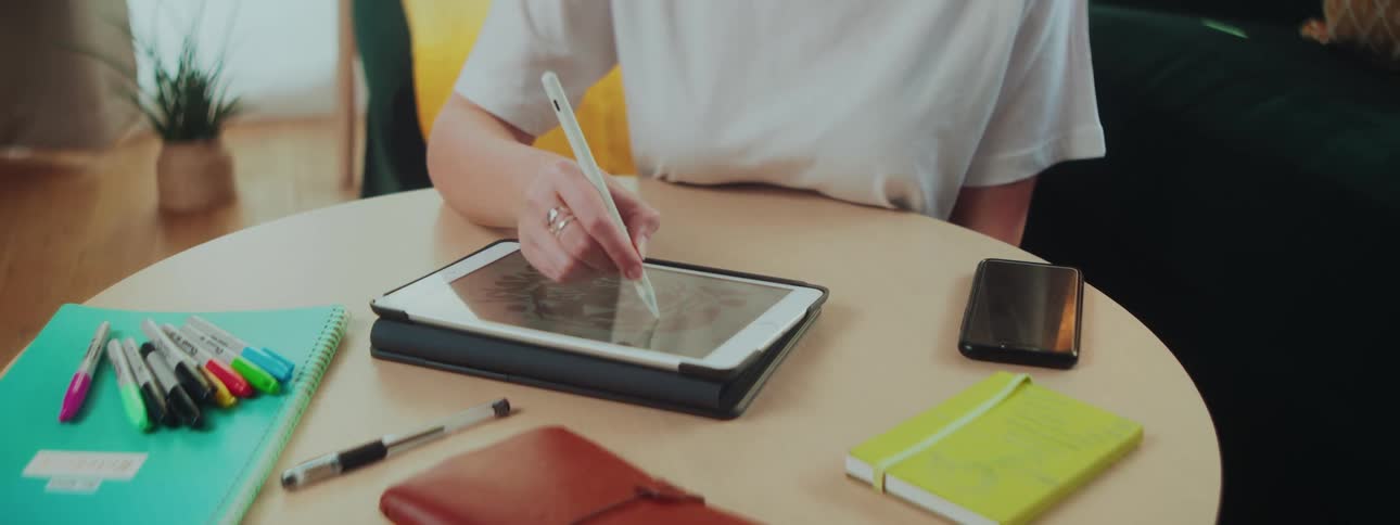 A woman sits on the floor in her living room writing with a pen on a coffee table
