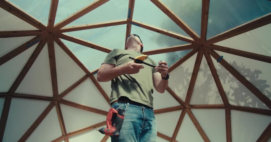 A man assembles a geodesic dome on a ladder in a suburban backyard focused on his work with tools