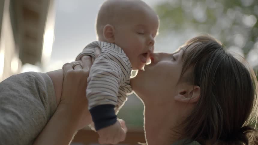 A mother is holding a baby up and giving it a kiss