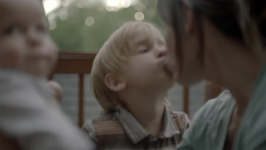 A mother is holding a baby and receiving a kiss from a young boy