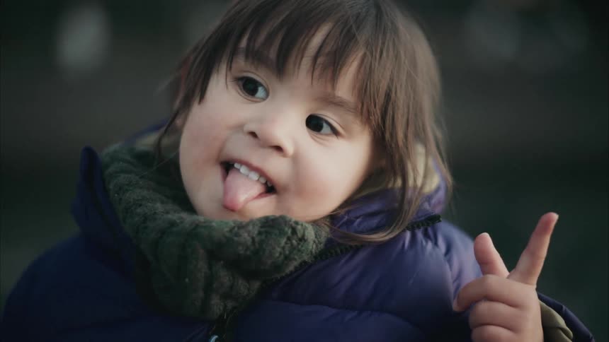 Young child bundled in winter clothing smiles and gestures playfully at the camera