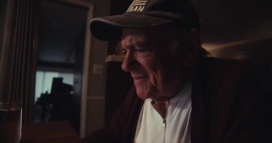 An older man sitting at a table in a living room typing on his laptop
