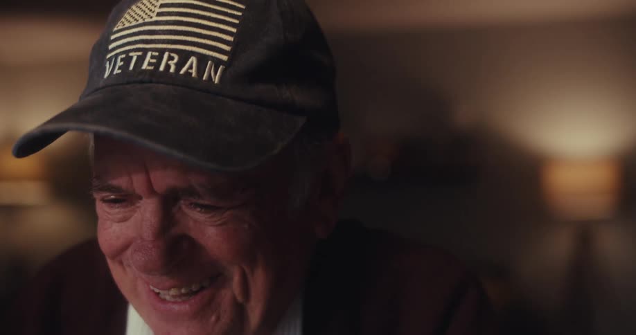 An elderly man smiles and laughs during a warm joyful video call in a cozy room