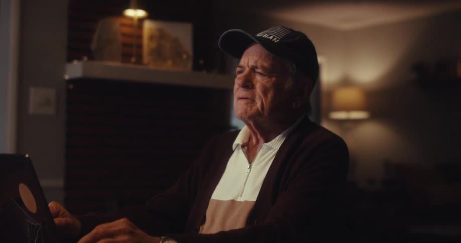 Elderly man using a laptop while sitting at home leans back in thought