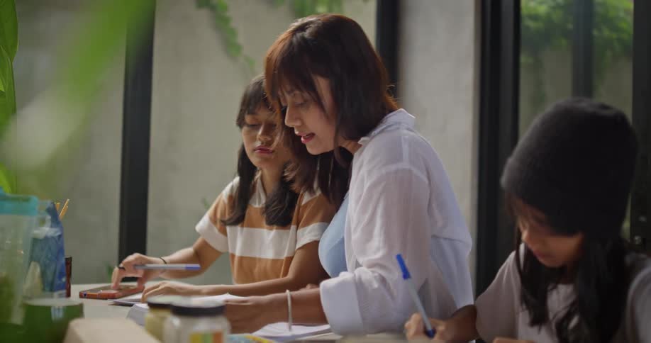A mother helps her two kids with homework at a kitchen table in a bright modern home