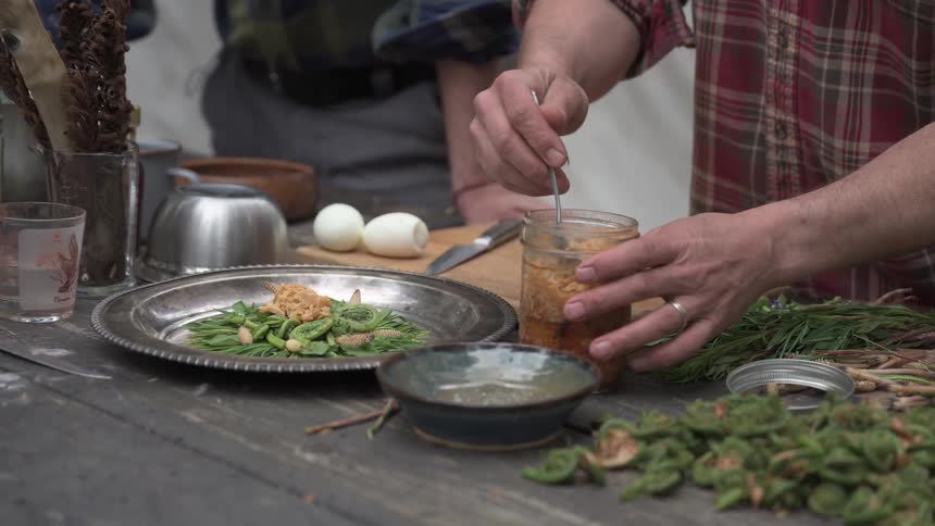 A man serves food from a jar onto a plate of vegetables on a dining table