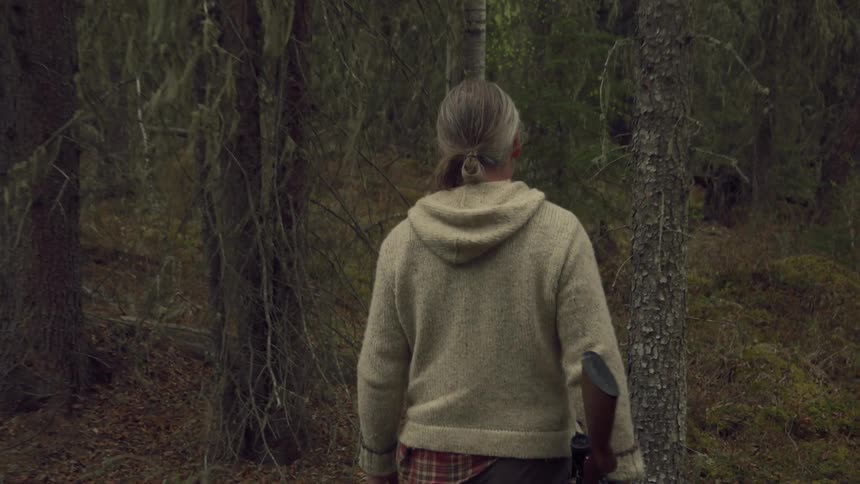 The man is hunting in the forest with a rifle