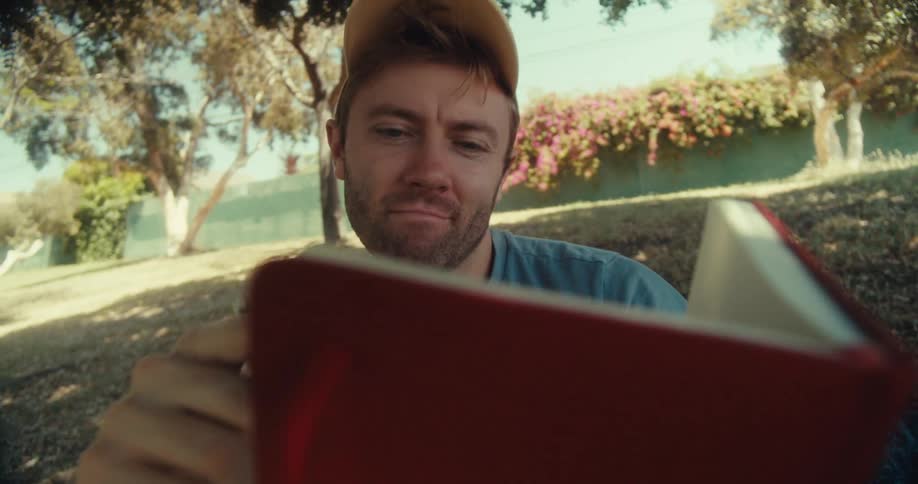 Man sitting on a blanket in the park during the daytime writes in a journal