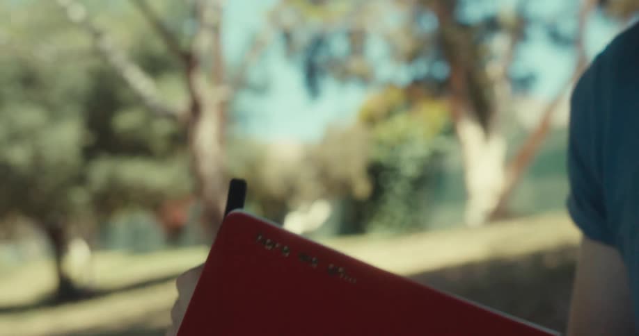 A man is sitting by a tree and writing in his notebook