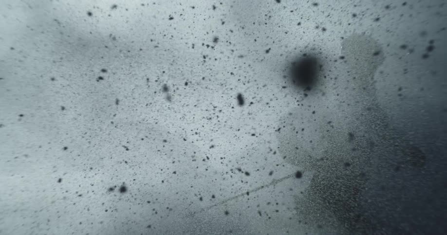A skier kicks up a spray of snow while moving downhill on a dark overcast day