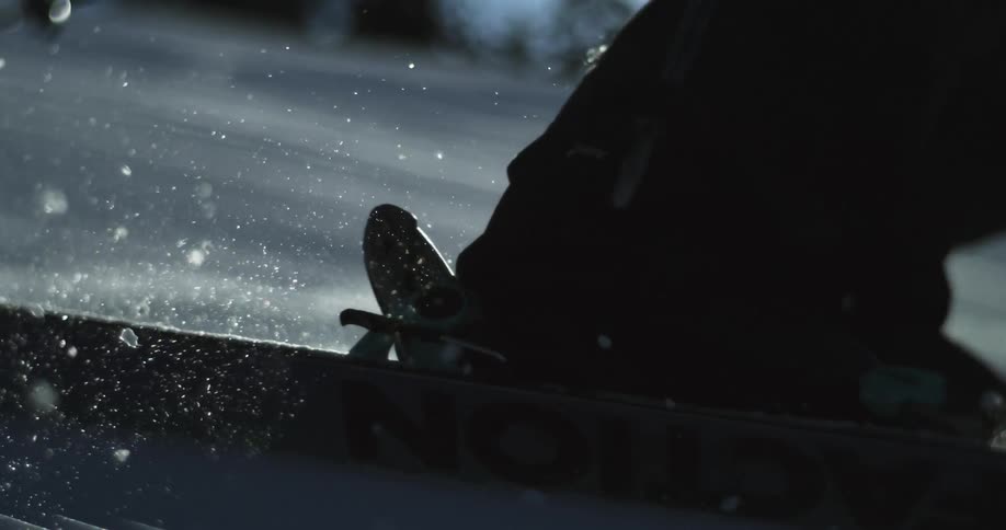 A skier glides over a textured snowy surface leaving a trail of glowing particles shining in the sun