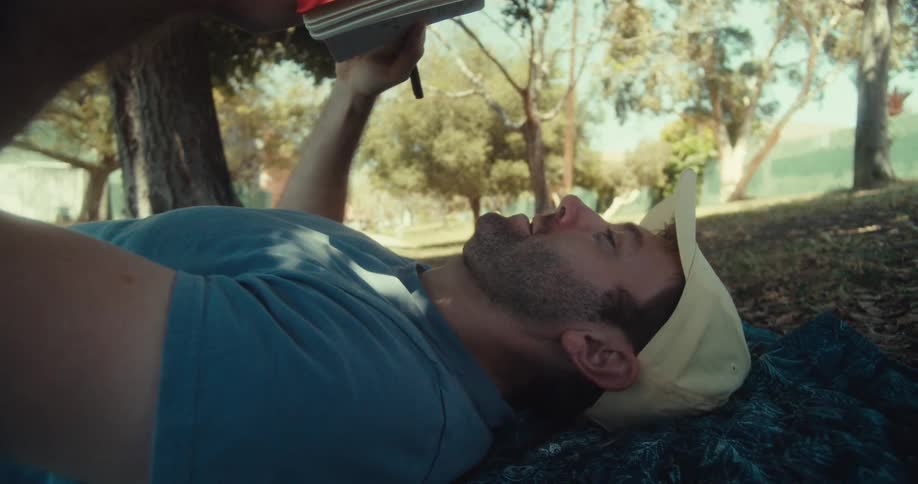 Man in cap lying on towel outdoors holding small notebook
