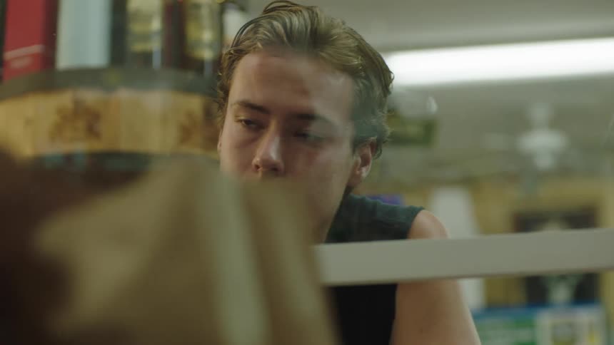 A young man waits for the cashier to put his groceries into a paper bag at check out