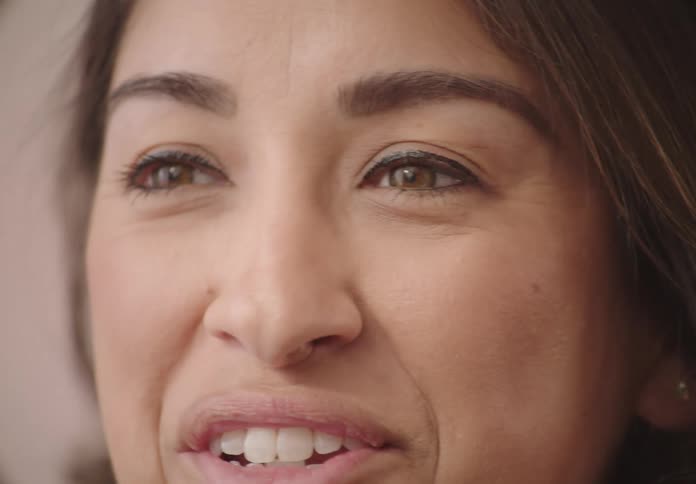 A closeup of a womans face talking to someone with a muted background
