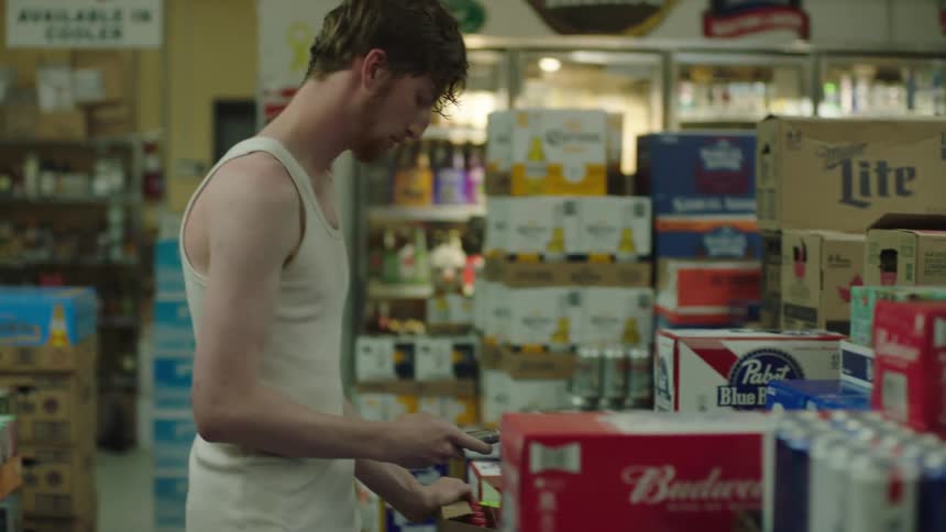 Two men in the aisle of a liquor store and another man using his smartphone