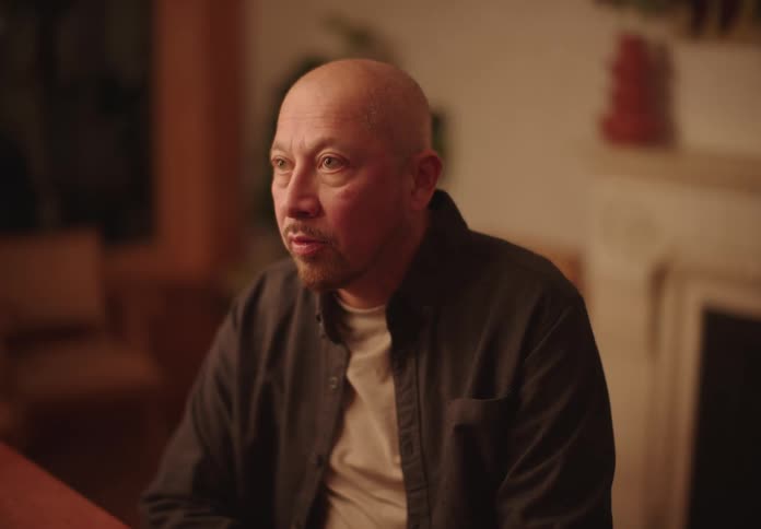 A bald man sitting at a table looking sad listening to someone
