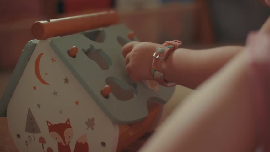 An infant plays with a toy indoors while wearing a watch